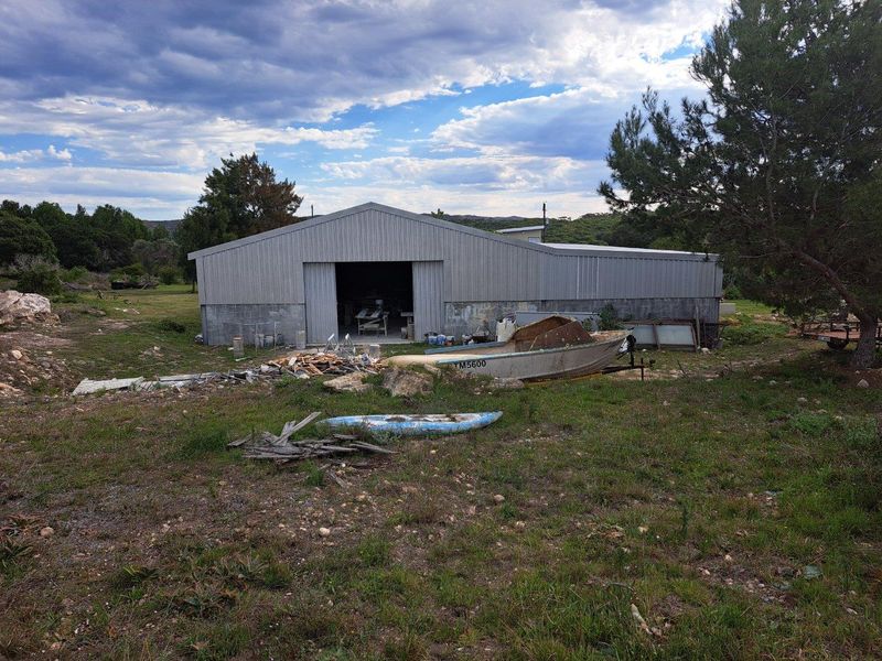 A large metal-clad farm shed or utility building situated on a rural property, featuring a wide sliding entrance and surrounding open land.