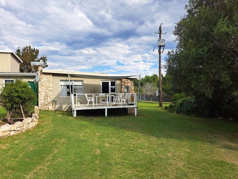 Rear view of the farm dwelling featuring a raised timber deck, stone cladding accents, and a spacious surrounding lawn area.