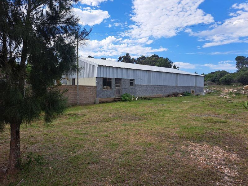 A view of a large, utilitarian farm outbuilding featuring corrugated metal roofing and concrete block walls, set within a spacious rural landscape.