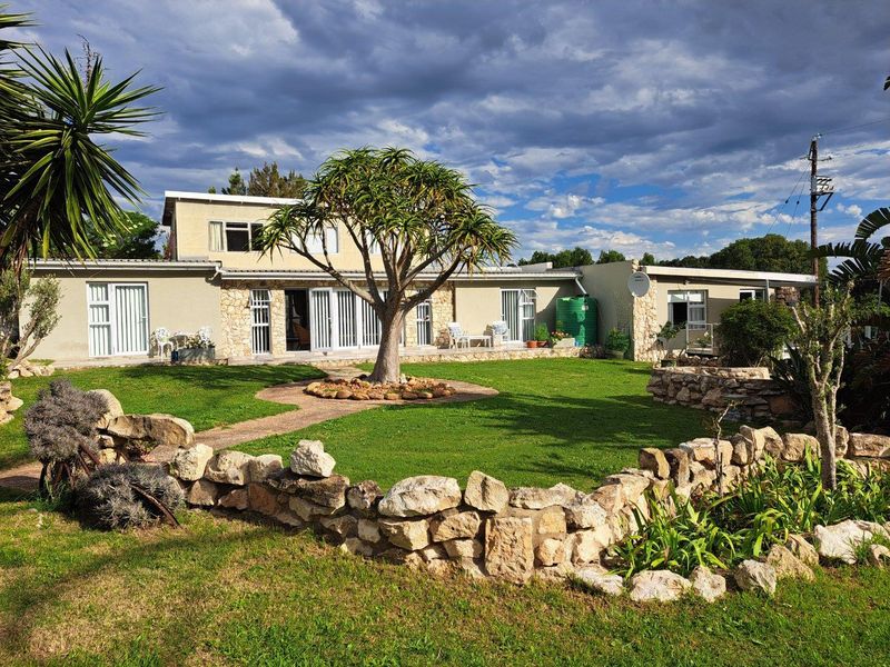Rear view of the farm property featuring a landscaped garden, stone retaining walls, and multiple glass sliding door access points to the main dwelling.