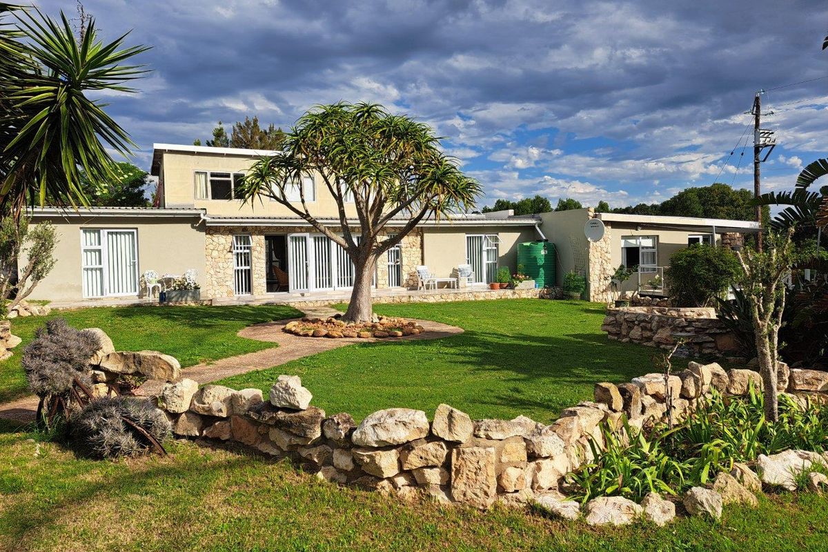 Rear view of the farm property featuring a landscaped garden, stone retaining walls, and multiple glass sliding door access points to the main dwelling.