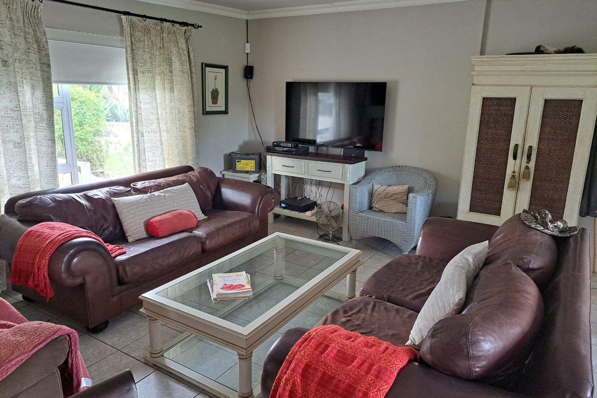 A comfortable living room featuring tiled flooring, a ceiling fan, and large windows providing natural light and garden views.