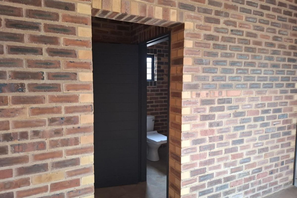 A view through a doorway into a bathroom featuring exposed brickwork walls and a standard toilet fixture.