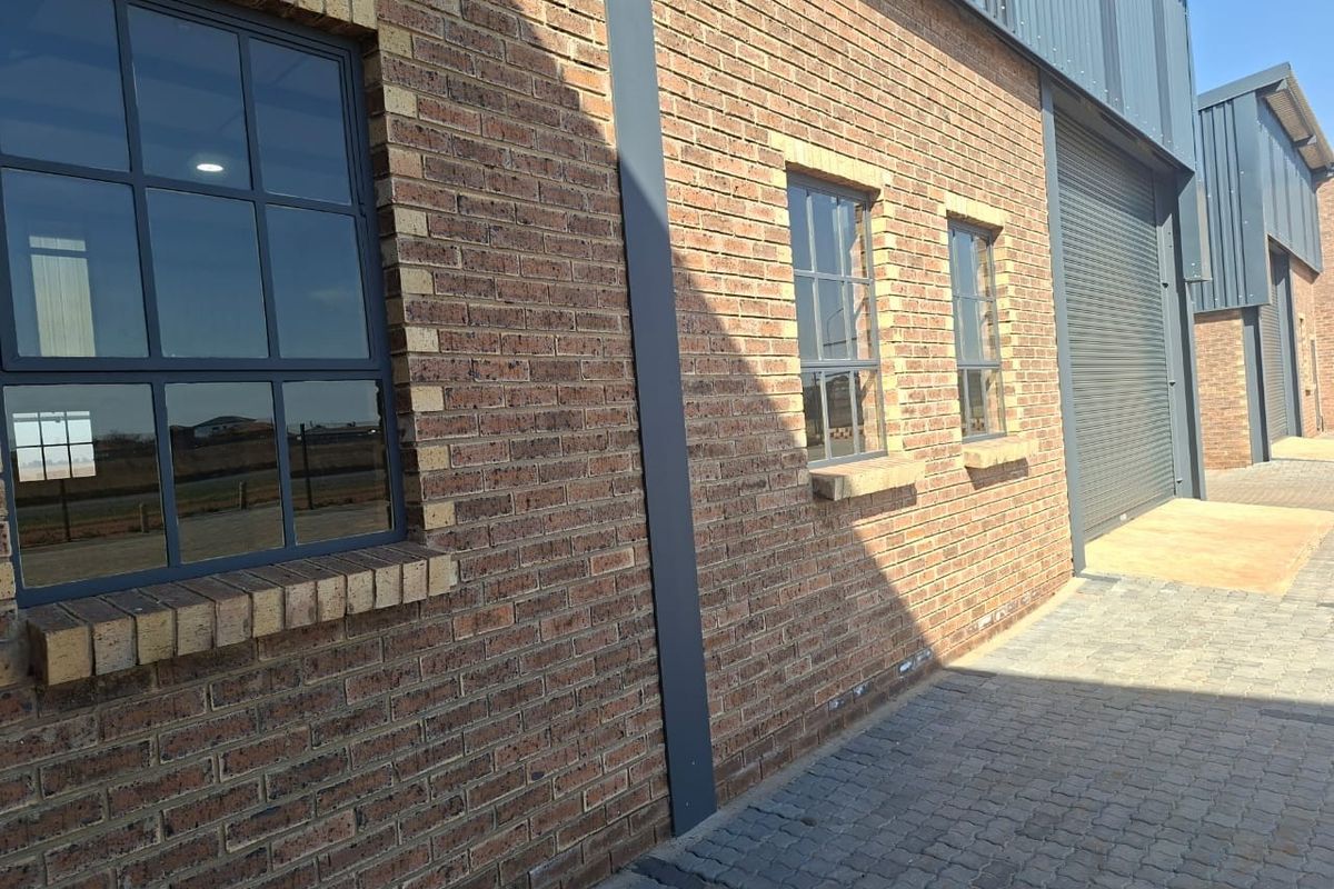 Exterior view of a modern commercial unit featuring face brick walls, steel-framed windows, and a secure roller shutter door with paved access.