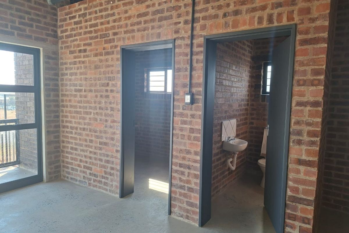 An industrial-style interior featuring exposed brick walls, polished concrete flooring, and a functional bathroom area with a wall-mounted basin and toilet.