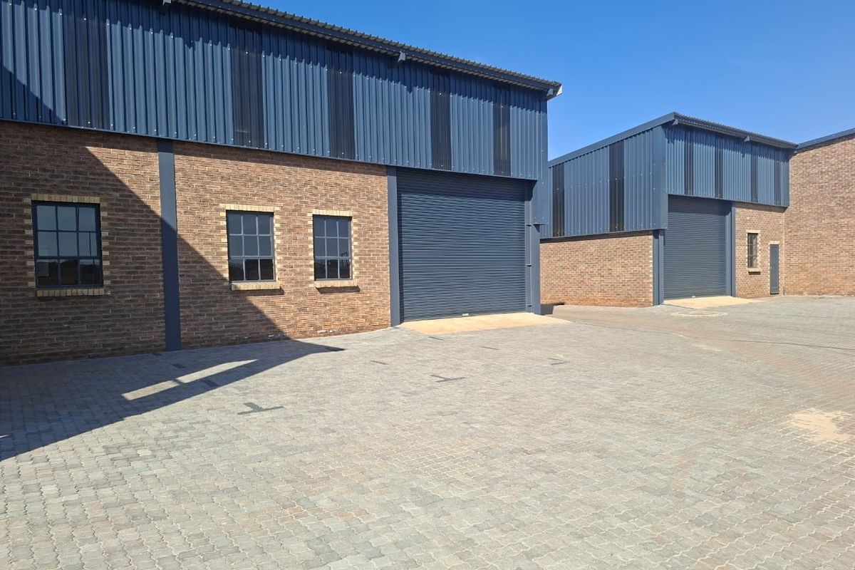 Modern commercial warehouse units featuring face brick exteriors, corrugated metal cladding, roller shutter doors, and a spacious paved driveway area.
