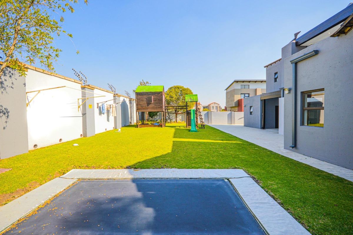 A spacious rear garden featuring a well-maintained lawn, paved walkway, perimeter wall with electric fencing, and an integrated in-ground trampoline.