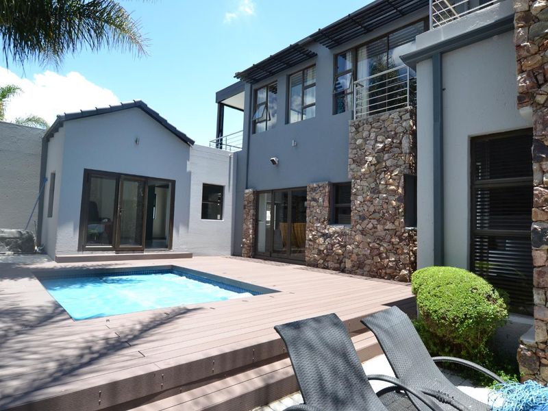 A modern rear exterior featuring a swimming pool, timber decking, and a multi-level facade with stone cladding and large sliding glass doors.