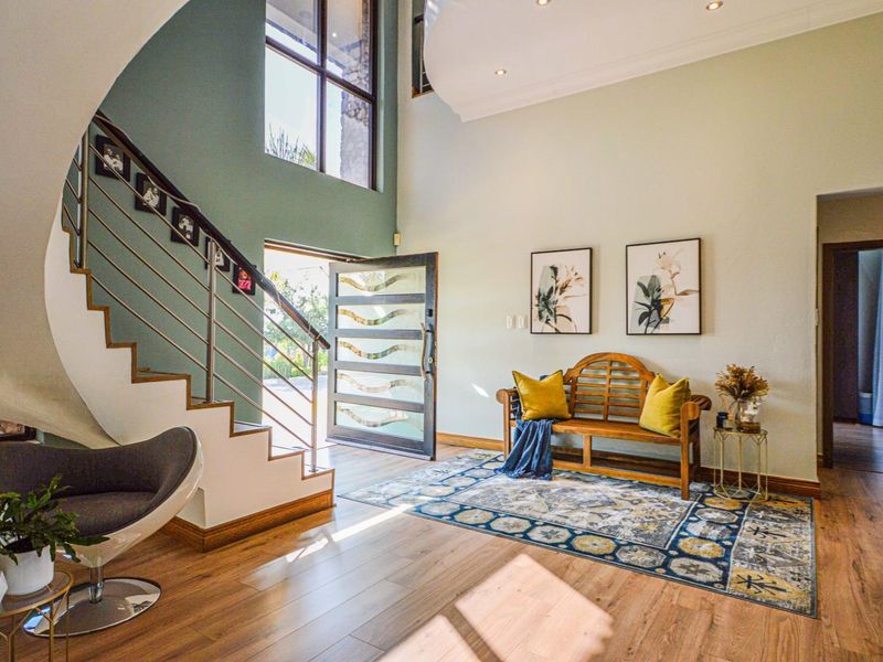 A grand double-volume entrance hall featuring a striking curved staircase, modern laminate flooring, and abundant natural light through a large feature window.