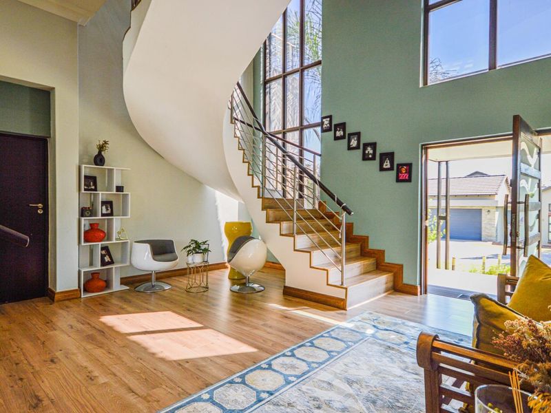 Spacious double-volume entrance hall featuring a striking curved staircase, modern laminate flooring, and large windows that provide abundant natural light.