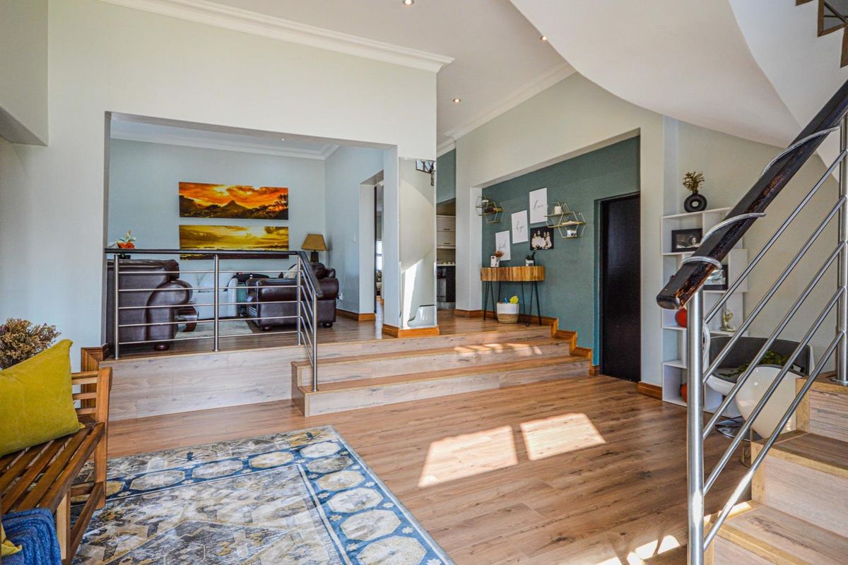 Spacious living area featuring a raised platform, modern laminate flooring, and a contemporary staircase with a stainless steel balustrade.