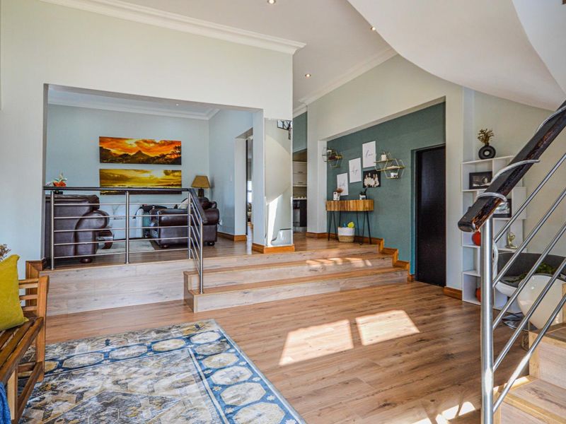 Spacious living area featuring a raised platform, modern laminate flooring, and a contemporary staircase with a stainless steel balustrade.