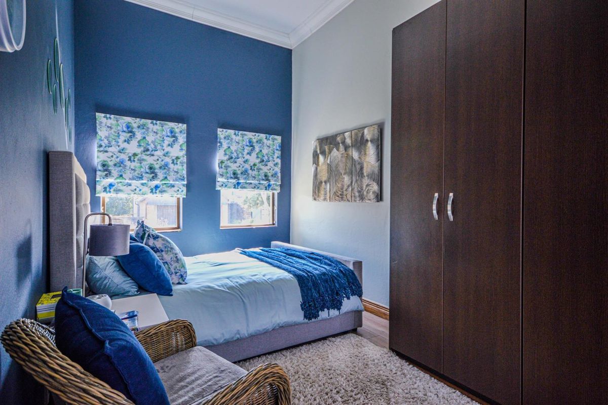 A well-maintained bedroom featuring a large built-in wardrobe, crown molding, and laminate flooring, finished with a bold blue accent wall.