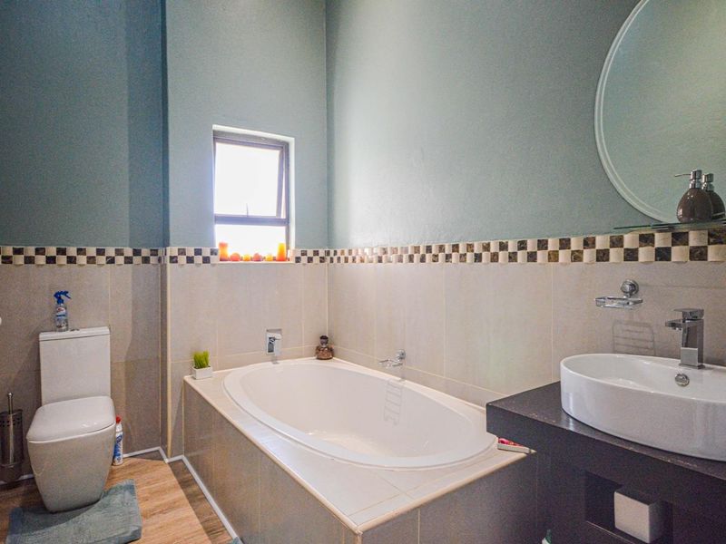 A functional bathroom featuring a built-in bathtub, a modern vessel sink on a vanity cabinet, and a toilet, finished with decorative tiled wall accents.