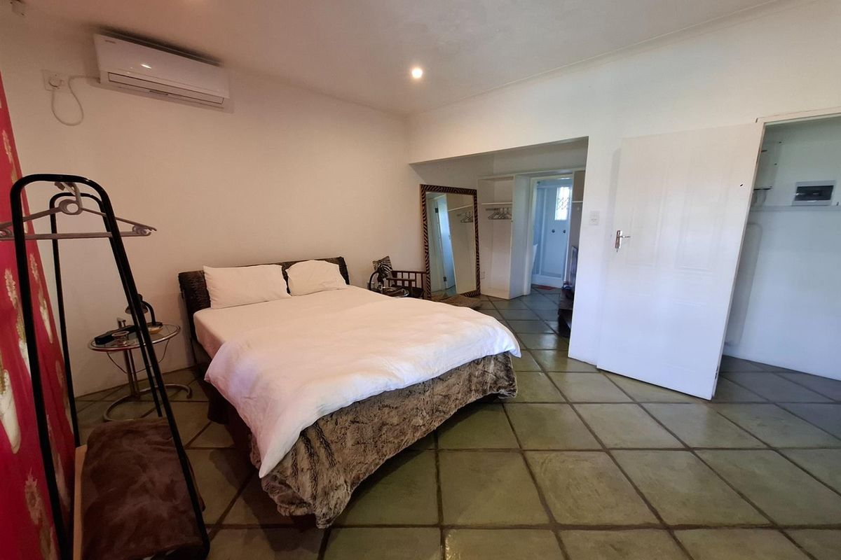 Spacious bedroom featuring tiled flooring, a wall-mounted split-system air conditioner, and direct access to an en-suite bathroom area.