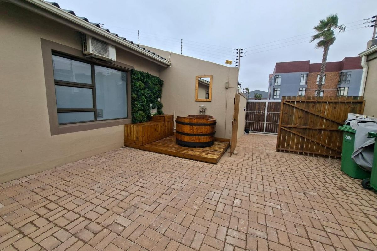 A paved rear courtyard featuring a wooden deck, a built-in wooden hot tub, and a vertical garden wall.