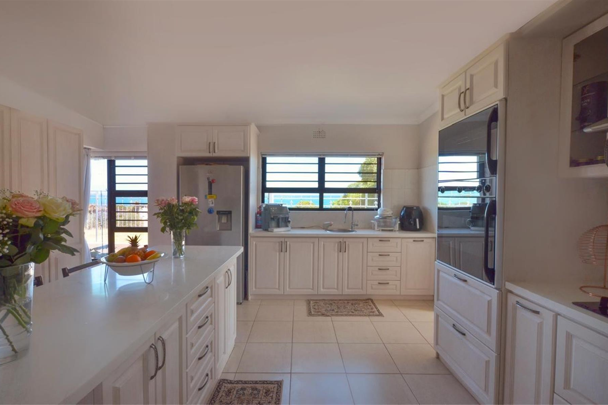 A bright, well-maintained kitchen featuring white cabinetry, a central island, tiled flooring, and built-in oven, with views through the window.