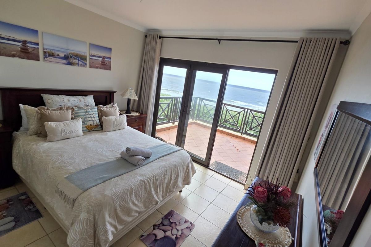 A well-maintained bedroom featuring tiled flooring, large sliding glass doors leading to a private balcony, and expansive ocean views.