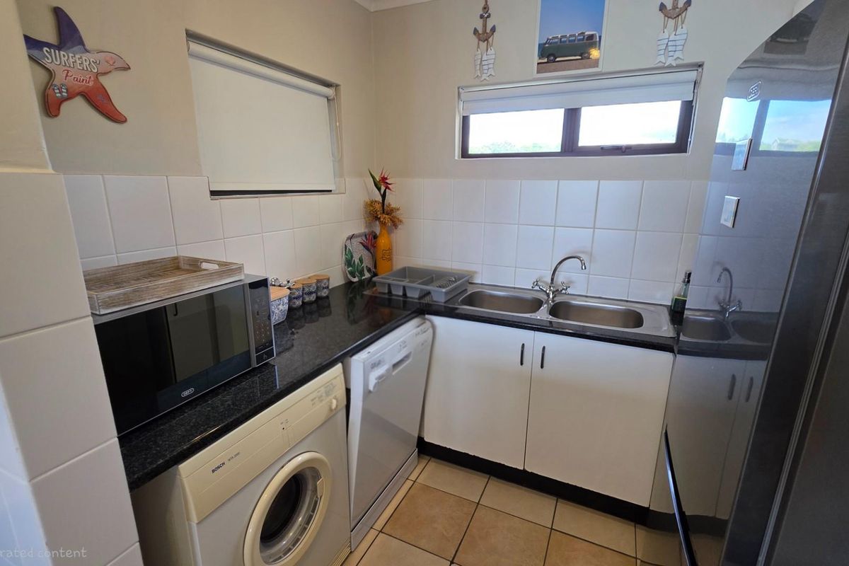 A functional kitchen and laundry area featuring dark granite countertops, white cabinetry, a double stainless steel sink, and tiled splashbacks.