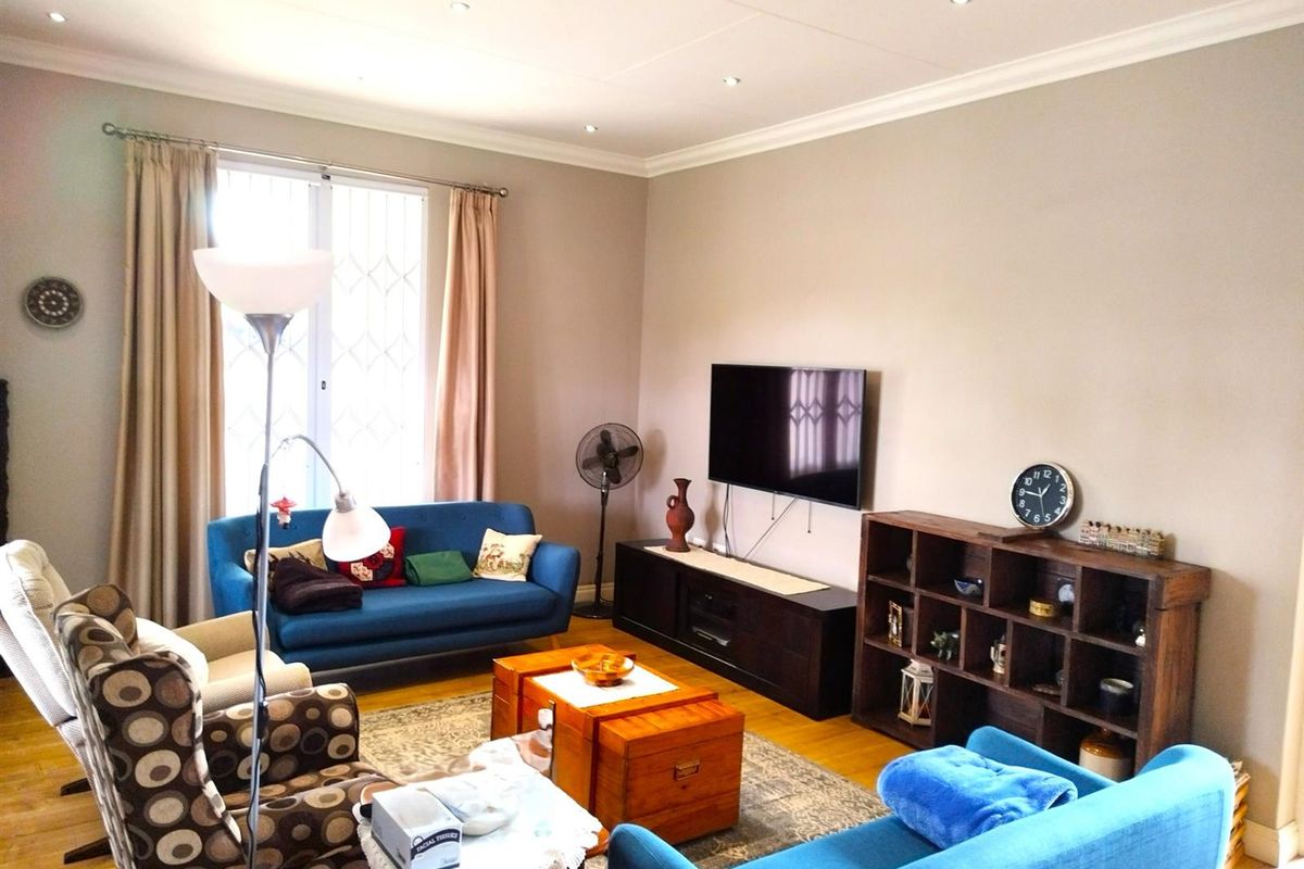 A comfortable living room featuring hardwood flooring, recessed ceiling lighting, and a large window with security bars.