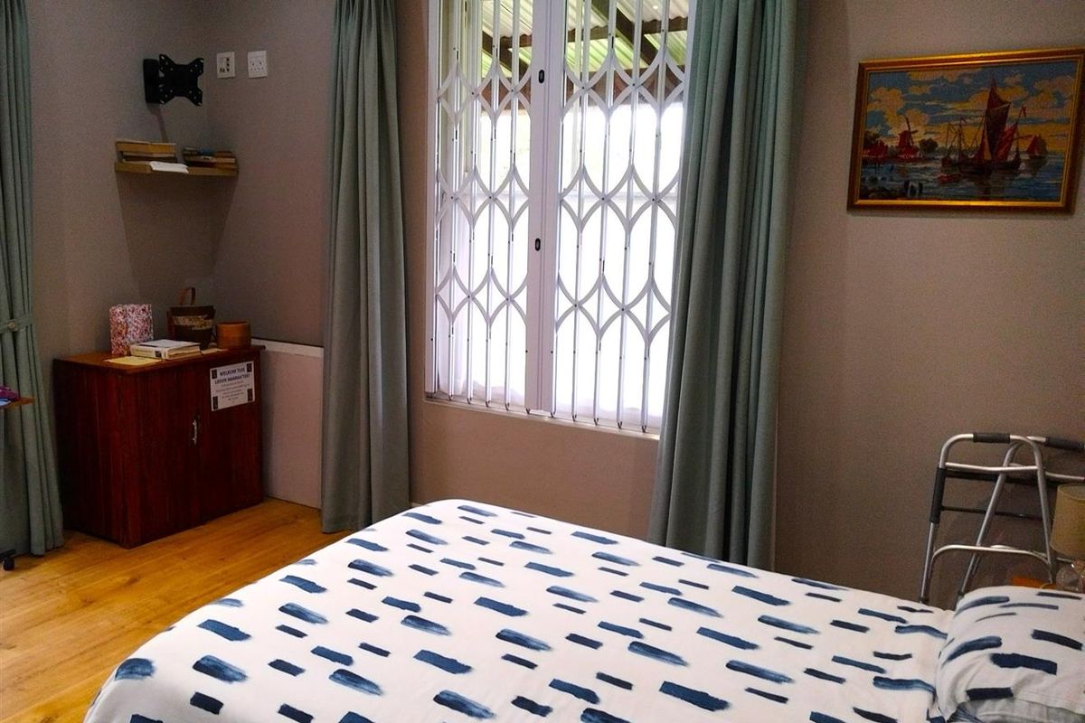 A well-maintained bedroom featuring laminate flooring, a window with security gate, and neutral wall tones.