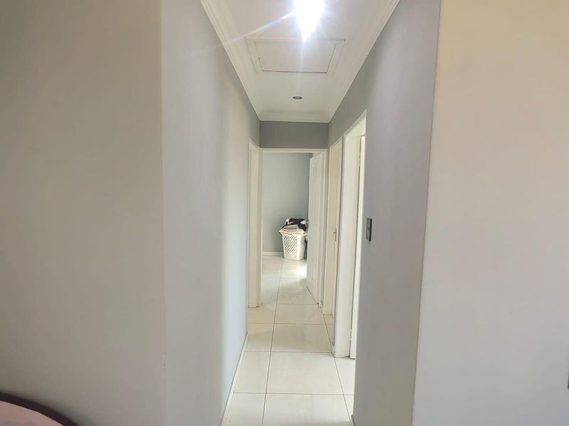 A bright, tiled hallway providing access to multiple rooms, featuring neutral wall tones and a ceiling access hatch.