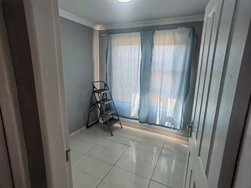 A compact bedroom featuring neutral grey walls, white tiled flooring, and crown molding, offering a clean and functional space.