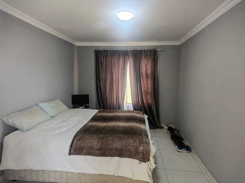 A bedroom featuring tiled flooring, crown molding, and a window dressed with curtains.
