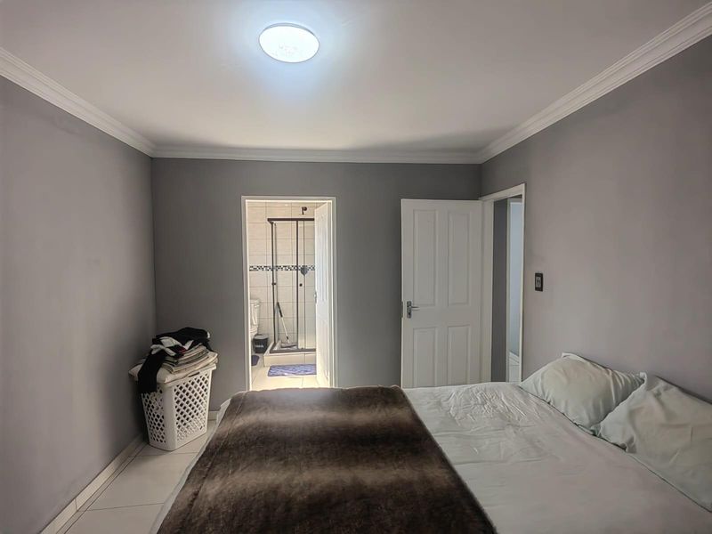 A bedroom featuring grey walls, crown molding, and an en-suite bathroom with a glass-enclosed shower.