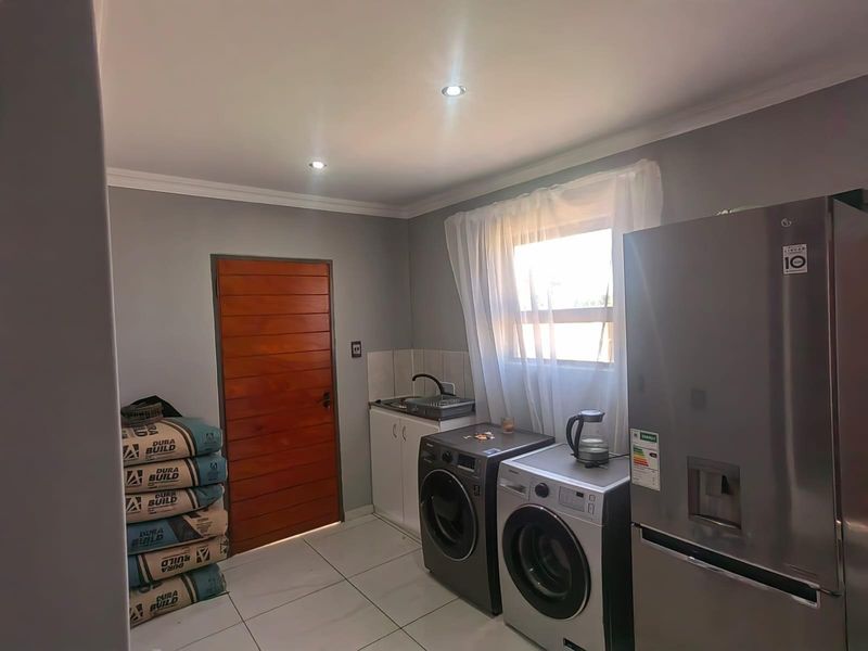 A functional laundry room featuring tiled flooring, built-in cabinetry with a sink, and space for laundry appliances.