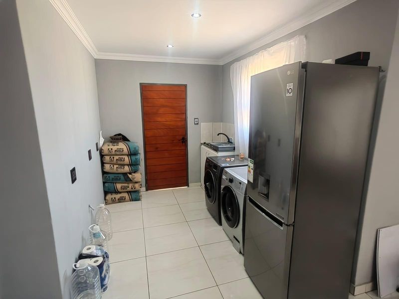 A functional laundry room featuring tiled flooring, recessed ceiling lighting, a small sink area, and dedicated space for laundry appliances.