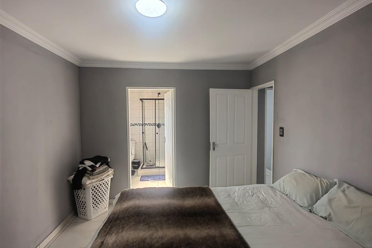 A bedroom featuring grey walls, crown molding, and an en-suite bathroom with a glass-enclosed shower.