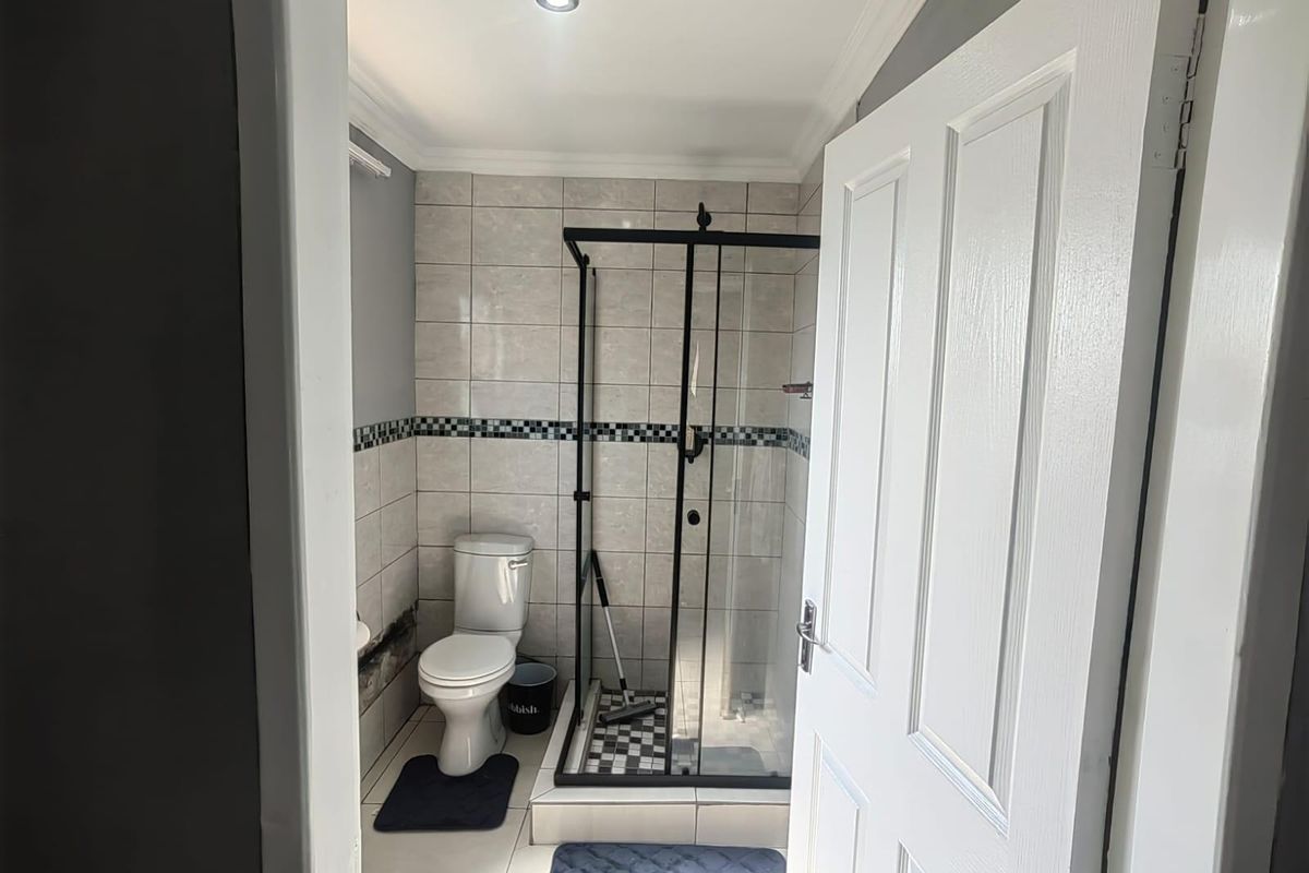 A compact bathroom featuring a glass-enclosed shower with black frame, a standard toilet, and neutral wall tiling with a decorative border.