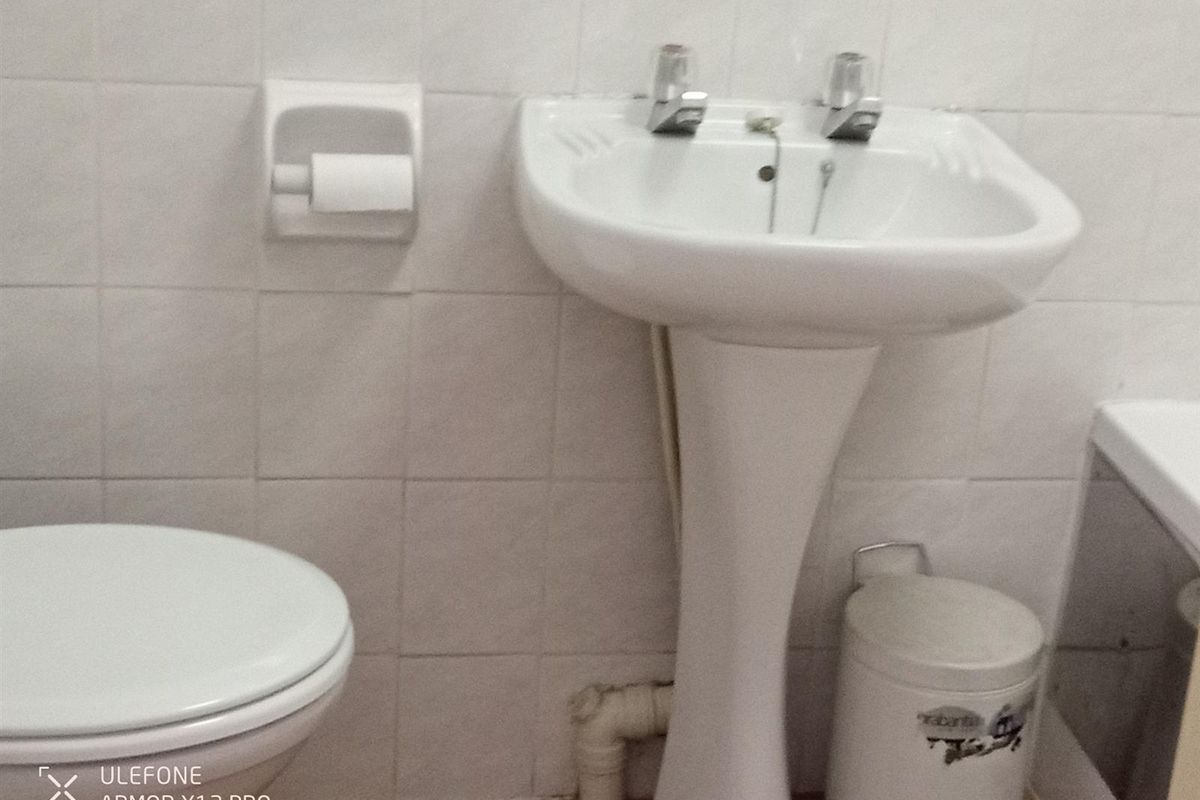 A functional bathroom featuring a white pedestal sink, toilet, and tiled walls.