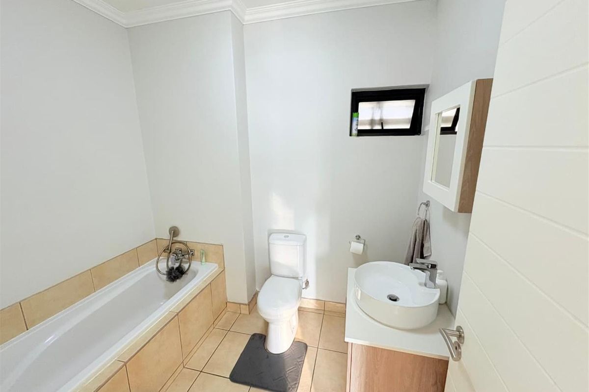 A clean, functional bathroom featuring a bathtub with tiled surround, a modern vessel sink on a vanity cabinet, and a standard toilet.