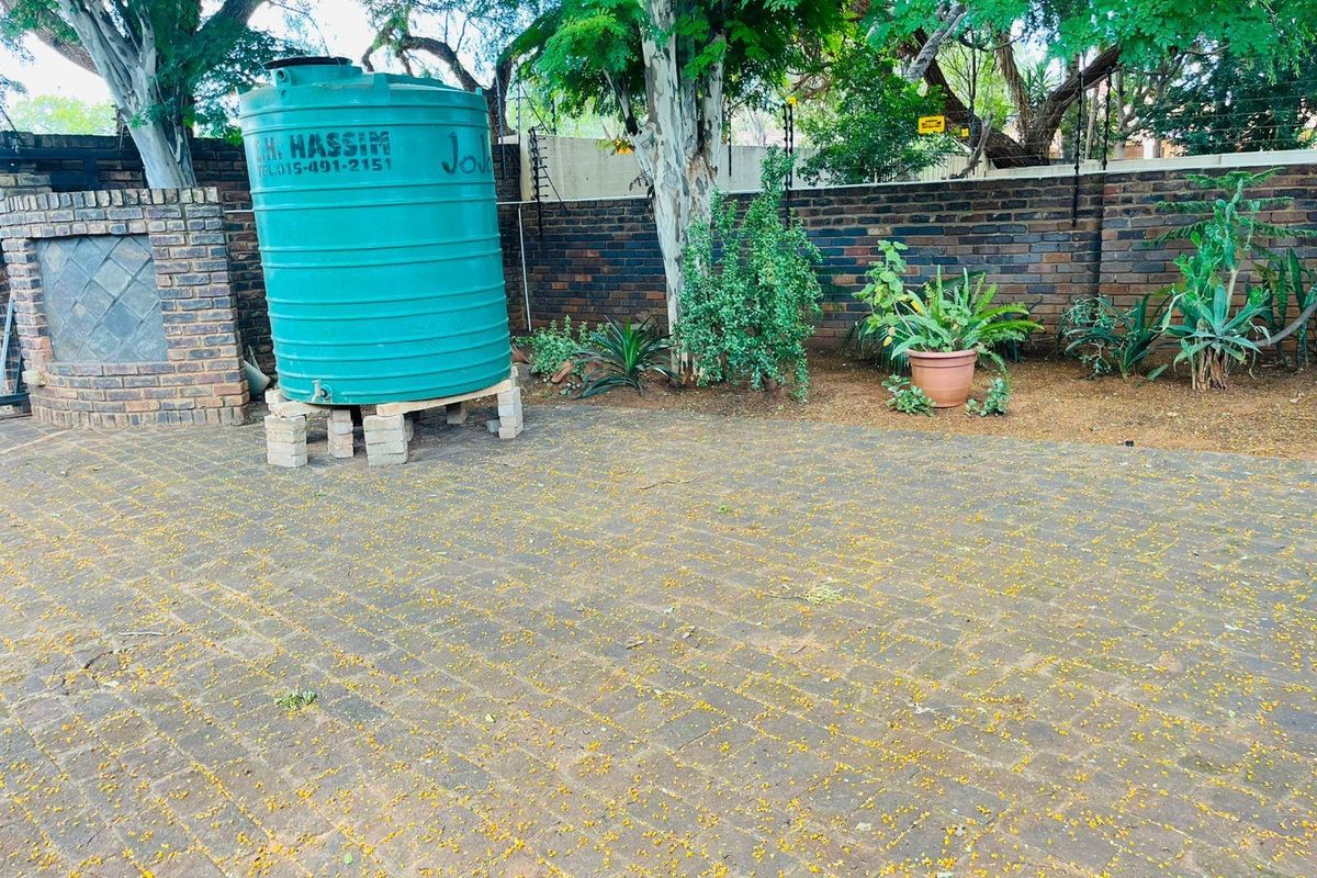 A paved outdoor area featuring a large green water storage tank, brick boundary wall, and established trees.
