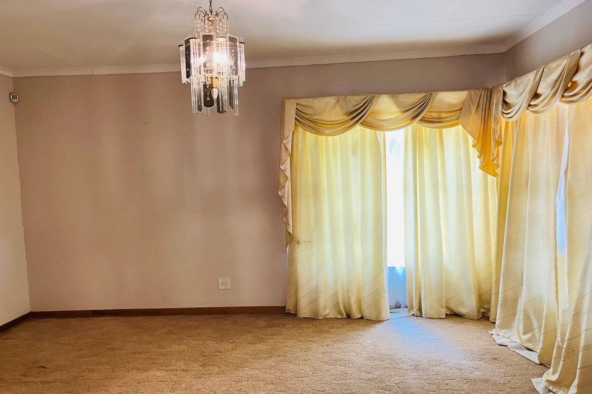 A spacious, empty living room featuring neutral walls, wall-to-wall carpeting, and a decorative crystal chandelier, offering a blank canvas for renovation.