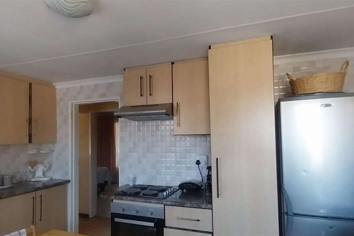 A functional kitchen featuring light wood-toned cabinetry, tiled splashbacks, a built-in oven with extractor fan, and ample storage space.