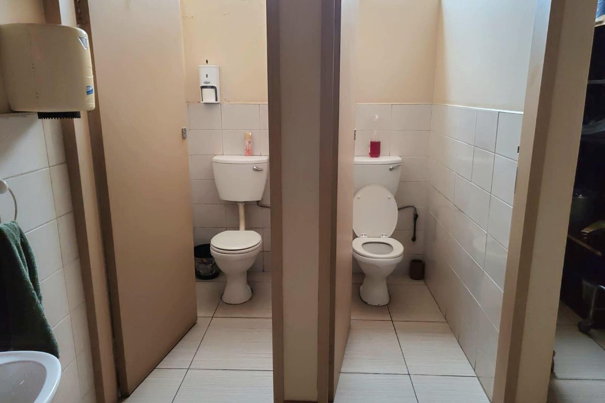 Commercial restroom facility featuring two individual toilet stalls with tiled walls and flooring, equipped with standard ceramic toilets and wall-mounted dispensers.