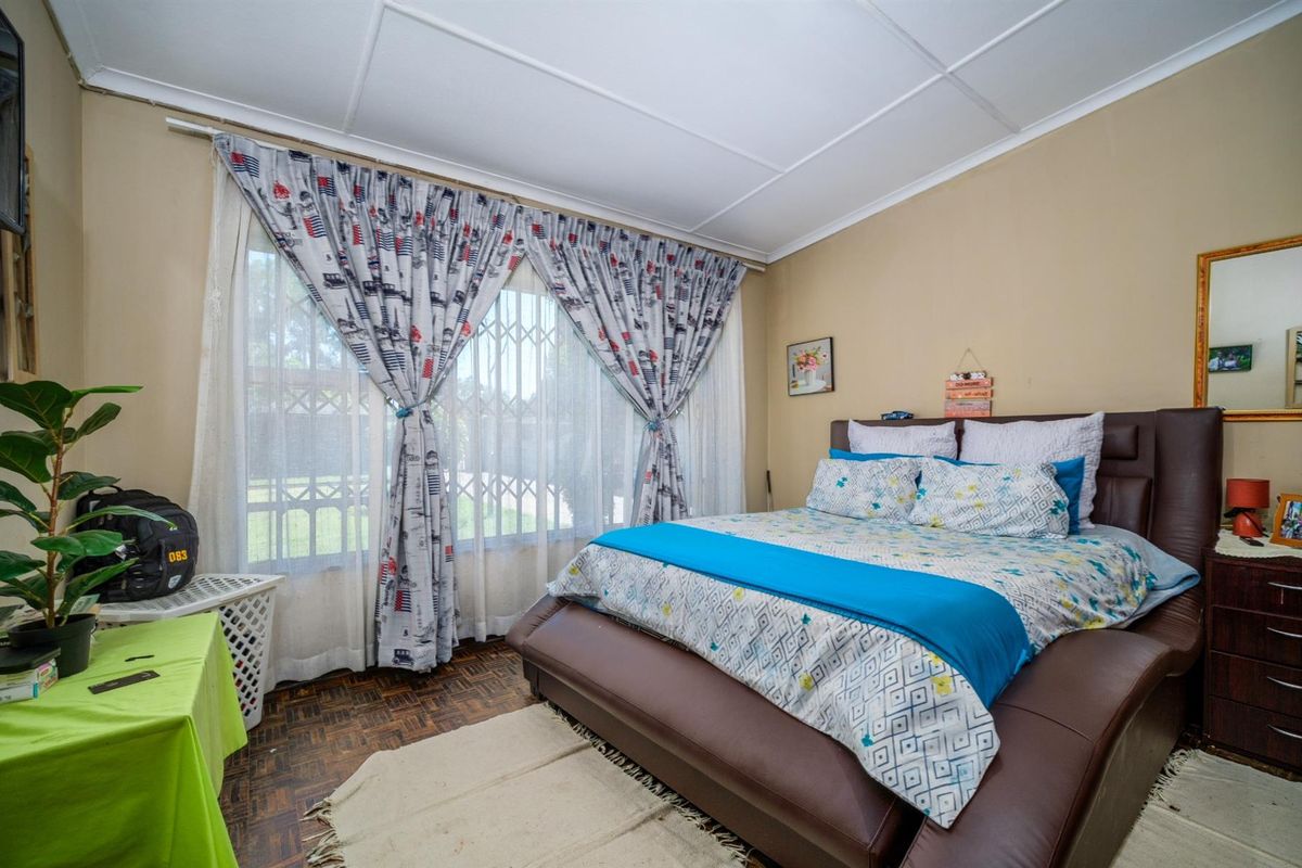 A bedroom featuring parquet flooring, large windows with security bars, and neutral wall finishes.
