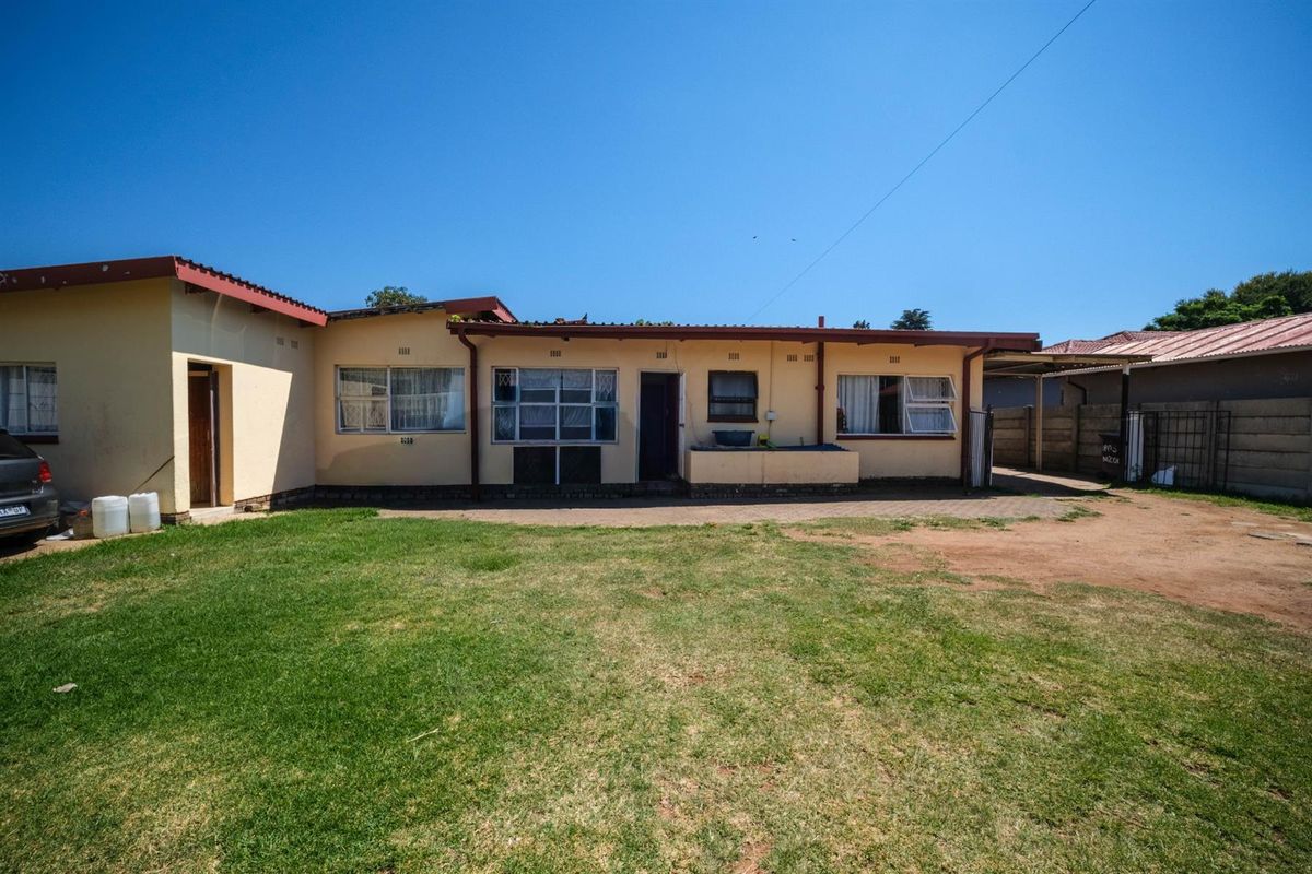 Rear view of the property featuring a paved patio area, lawn, and covered carport structure.