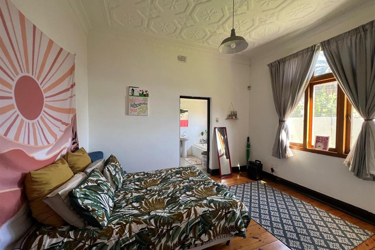 Spacious bedroom featuring original pressed metal ceilings, warm timber flooring, and a large window, with direct access to an adjoining bathroom.