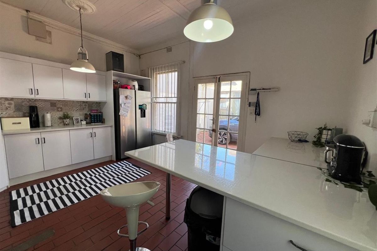 A functional kitchen featuring white cabinetry, a central island, tiled flooring, and direct access to the exterior through glass-paned french doors.