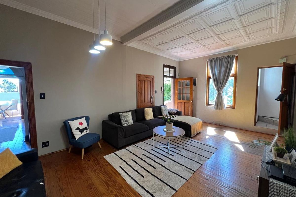 Spacious living room featuring original timber flooring, a decorative coffered ceiling, and natural light through timber-framed windows.