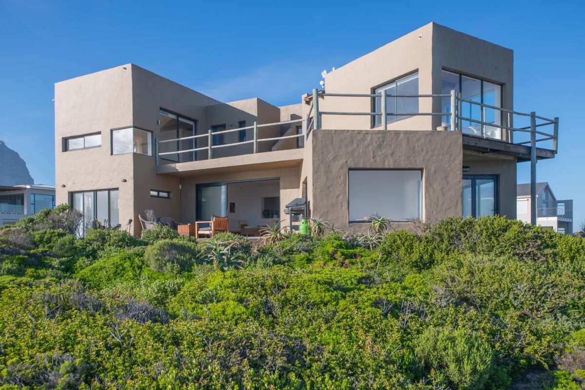 Rear view of a modern multi-level house featuring a stucco facade, expansive windows, and a spacious balcony overlooking the surrounding coastal landscape.
