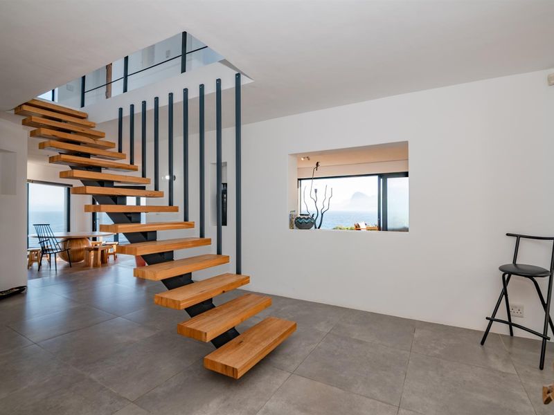 Modern open-plan hallway featuring a striking floating timber staircase with metal balustrades and large format floor tiles, offering views through an internal window.