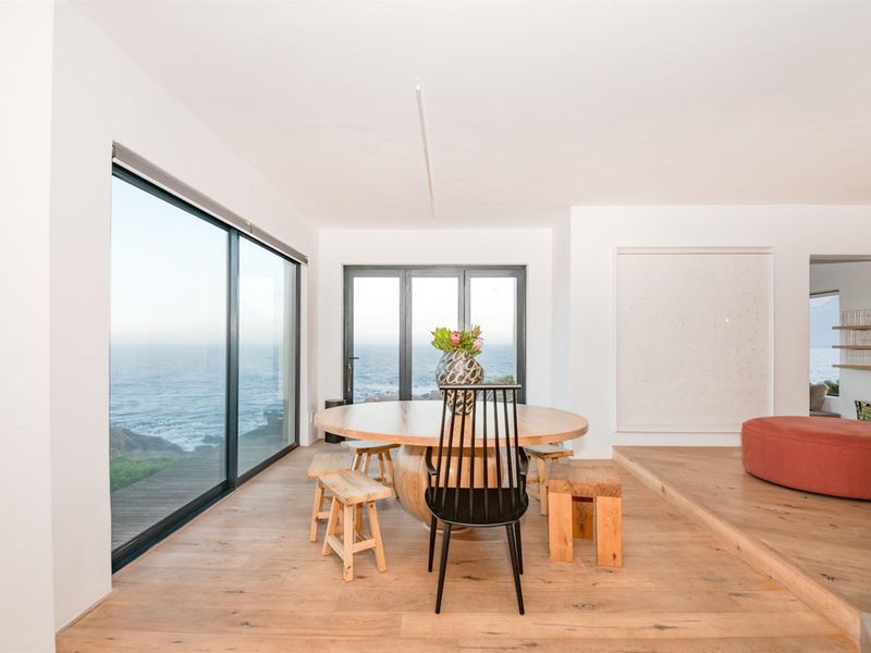 Bright dining area featuring timber flooring, a raised platform, and expansive sliding glass doors offering panoramic ocean views.
