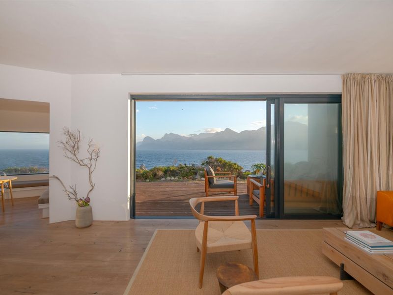 Bright living room featuring expansive sliding glass doors that open to a wooden deck with stunning ocean and mountain views.