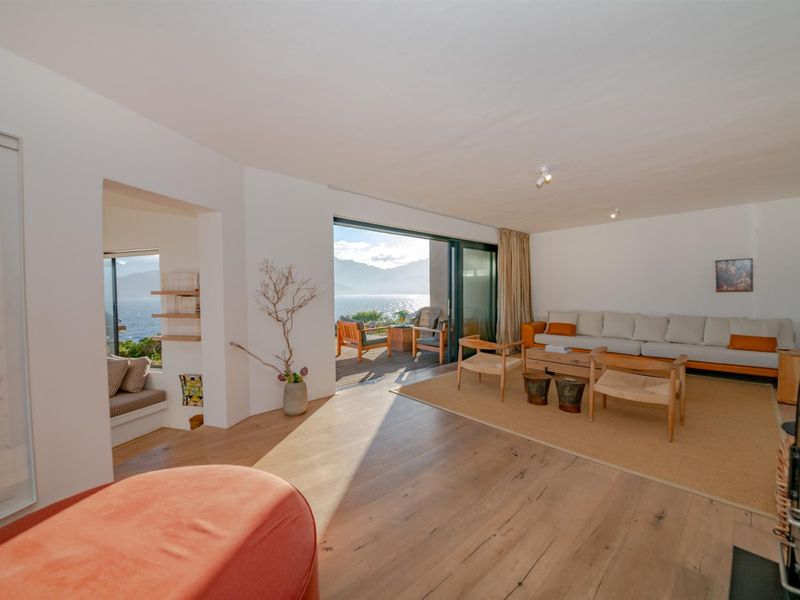 Spacious living room featuring hardwood flooring, a built-in fireplace, and large sliding glass doors opening to a scenic outdoor deck with water views.