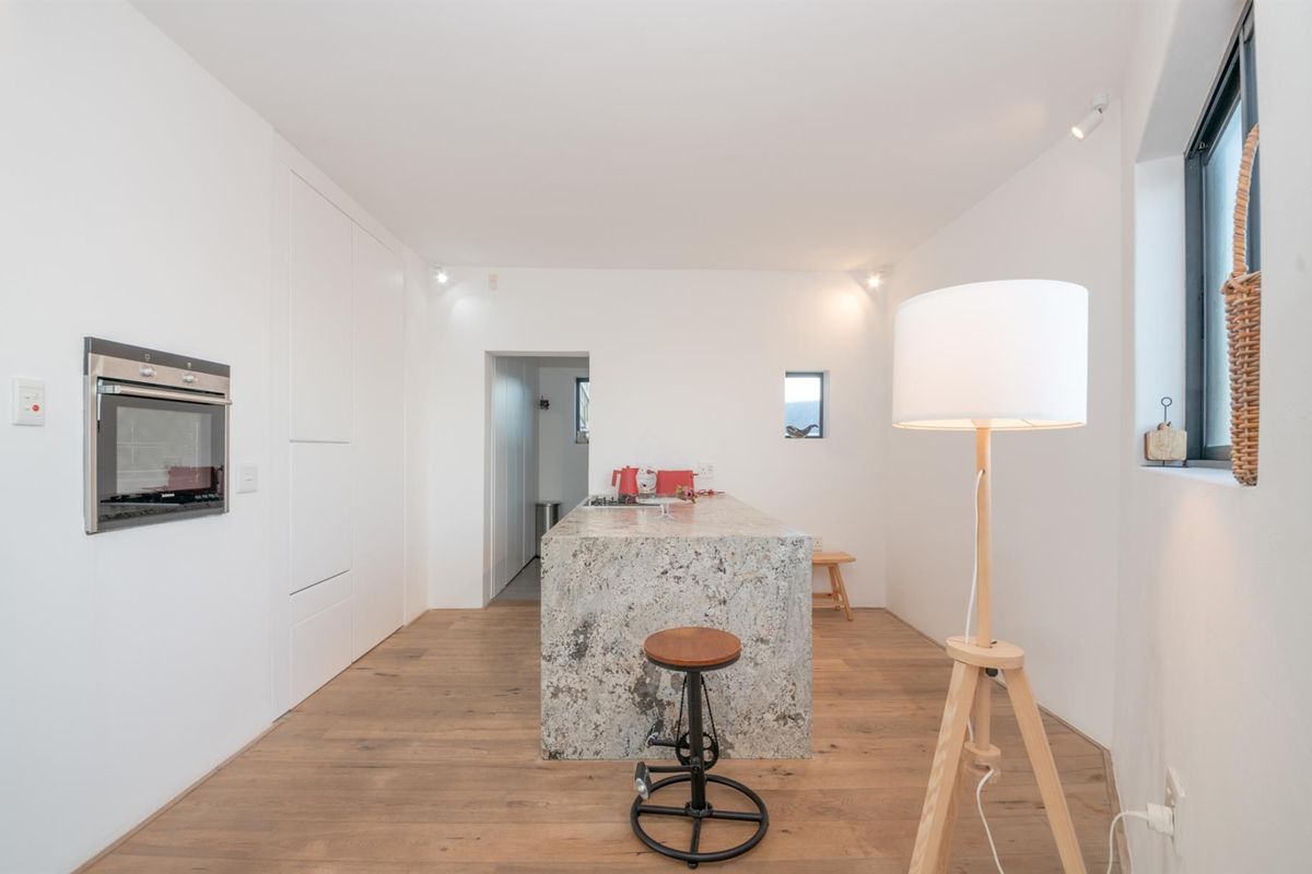Modern kitchen featuring a central stone island, built-in oven, integrated cabinetry, and warm hardwood flooring in a clean, minimalist design.